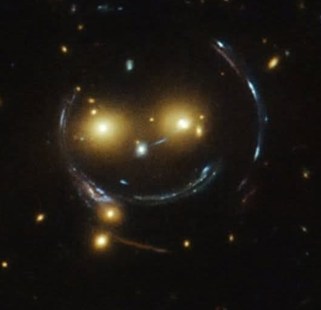 A galaxy cluster resembling a smiling face, ringed by gravitationally lensed arcs